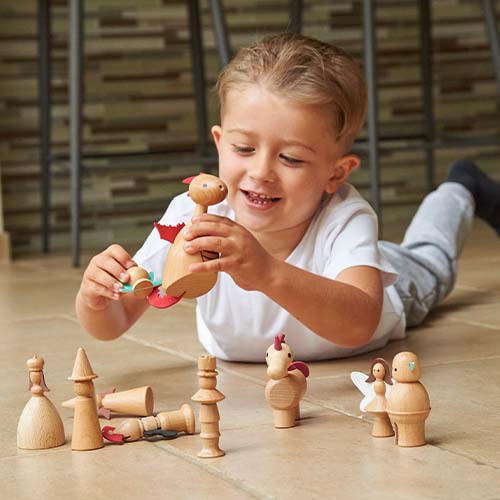 Een lachende jongen speelt met de tickit houten sprookjesfiguren en houdt de draak vast.