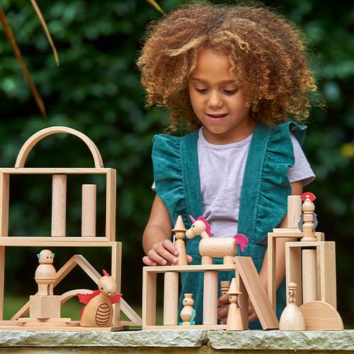 Een meisje speelt met de tickit houten sprookjesfiguren en houten bouwblokken buiten.