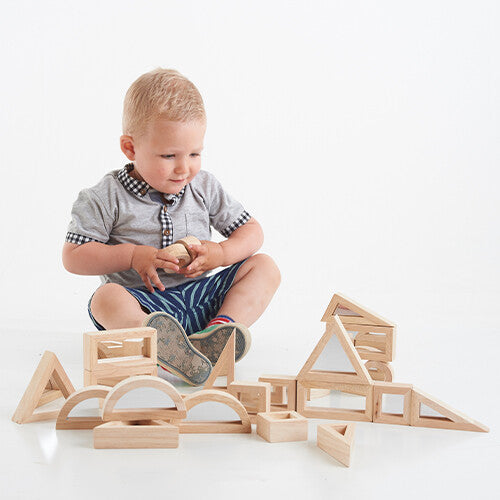 Een baby speelt op de grond met tickit houten spiegelblokken.