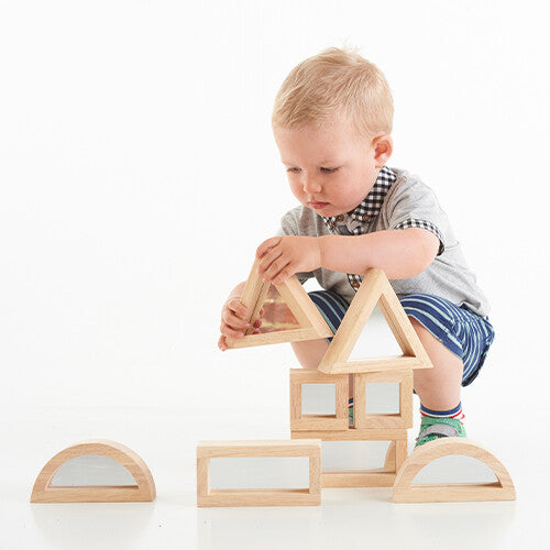 Een baby hurkt en speelt met tickit houten spiegelblokken, een driehoekig blok vasthoudend.