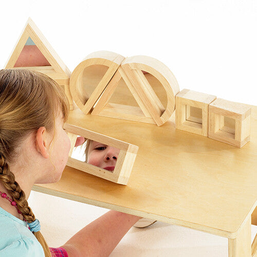 Een kind kijkt in een rechthoekig tickit houten spiegelblok, met andere blokken op een houten tafel.