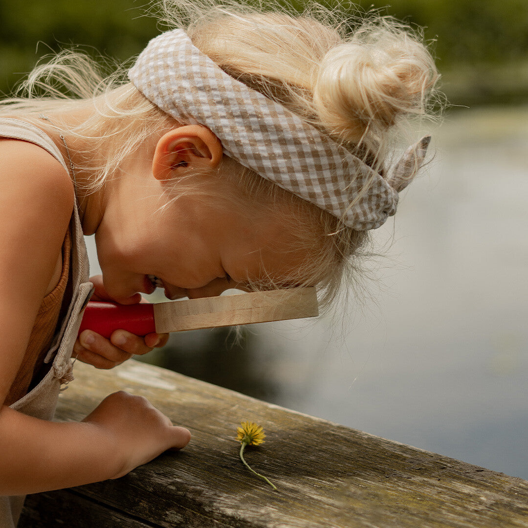 Kind onderzoekt een paardenbloem met een Tickit houten vergrootglas.