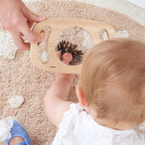 Een baby reikt naar het Tickit houten vergrootglas dat een dennenappel vergroot toont.