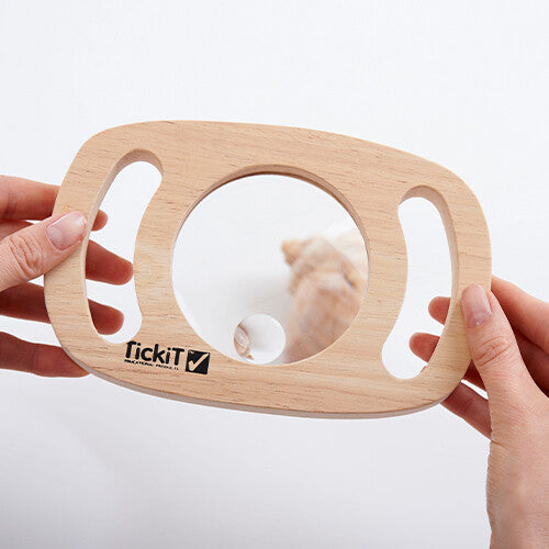 Twee handen houden het Tickit houten vergrootglas vast, dat een vergrote schelp toont.