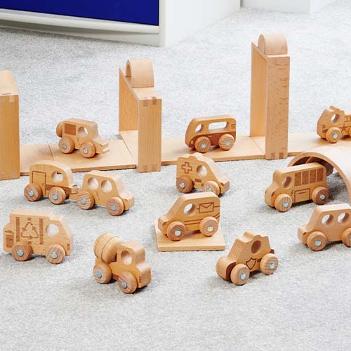 De tickit houten speelgoedvoertuigen staan op een grijs tapijt tussen houten bouwblokken.
