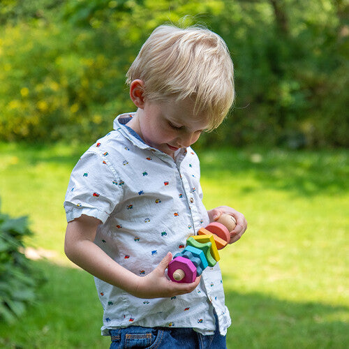 Een jongen houdt de tickit houten vormen twister met regenboogkleurige vormen vast in een tuin.