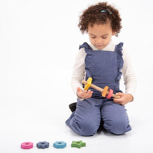 Een meisje knielt en kijkt naar de tickit houten vormen twister met losse regenboogkleurige vormen op de grond.