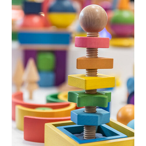 De tickit houten vormen twister staat rechtop tussen ander kleurrijk houten speelgoed.