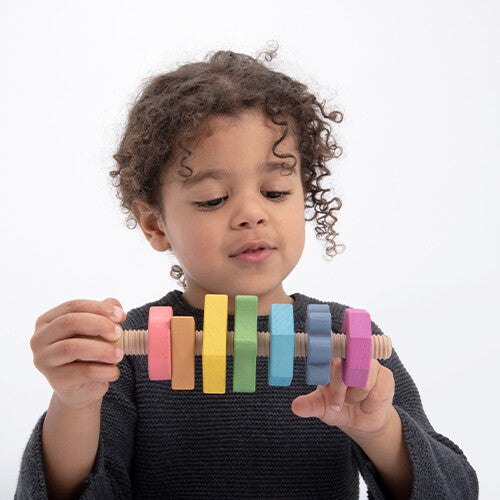 Een kind houdt de tickit houten vormen twister vast en draait aan de regenboogkleurige vormen.