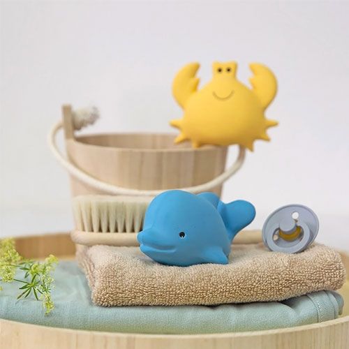 Tikiri blauw dolfijn bijt- en badspeelgoed met een geel krabje, een houten emmer en andere babyartikelen op een dienblad.