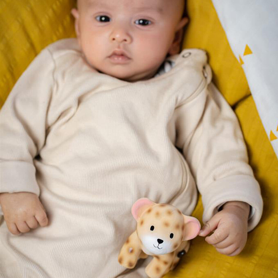 Een baby ligt op een gele deken met het Tikiri luipaard bijtspeelgoed naast zich.