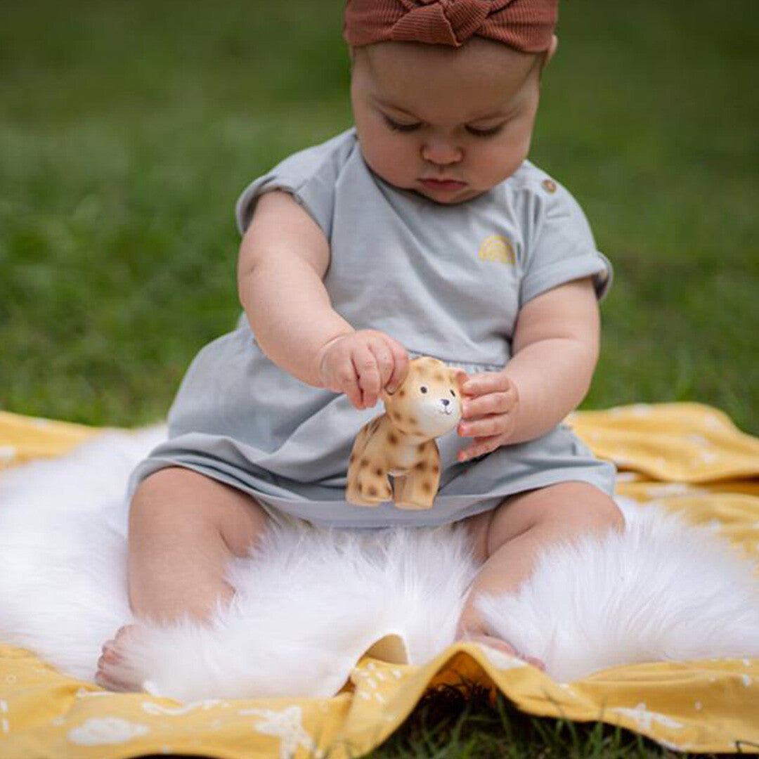 Een baby zit buiten op een kleed en speelt met het Tikiri luipaard bijtspeelgoed.