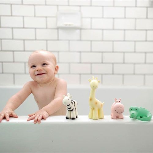 Een lachende baby in bad met vier tikiri bijt- en badspeeltjes op de rand van het bad.