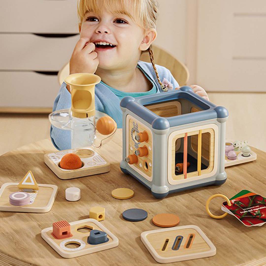 Lachende peuter speelt met de Topbright activiteitenkubus en losse vormen op een houten tafel.