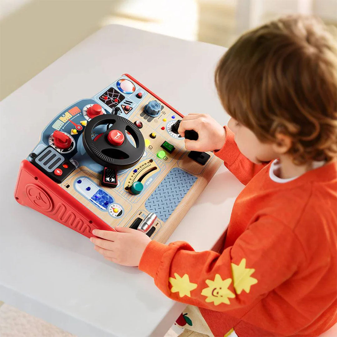 Een kind speelt met het Topbright activiteitenpaneel Fire Fighter, een houten speelgoedstuur met diverse knoppen en hendels, op een witte tafel.