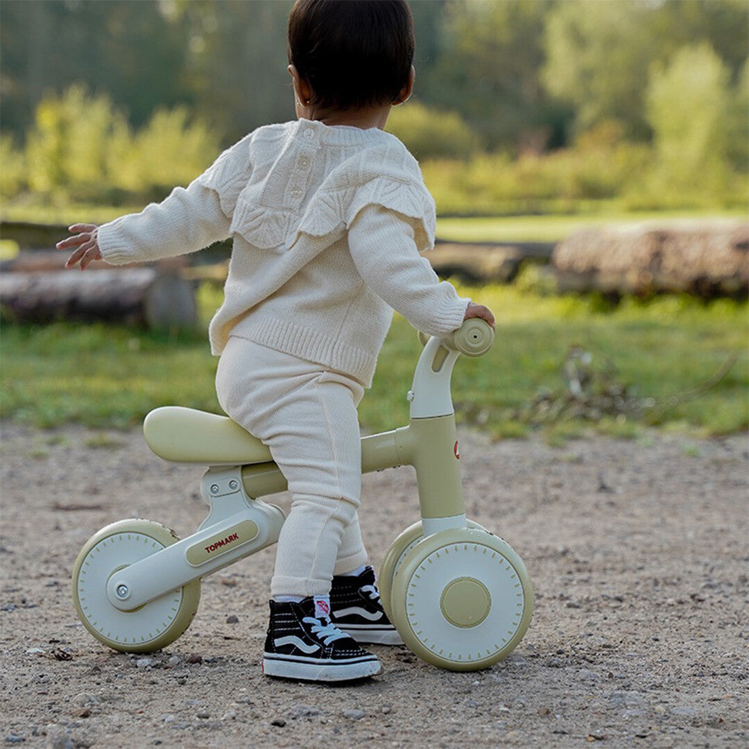 Een baby zit van achteren gezien op de Topmark loopfiets Yuki in pistachekleur, buiten op een pad.