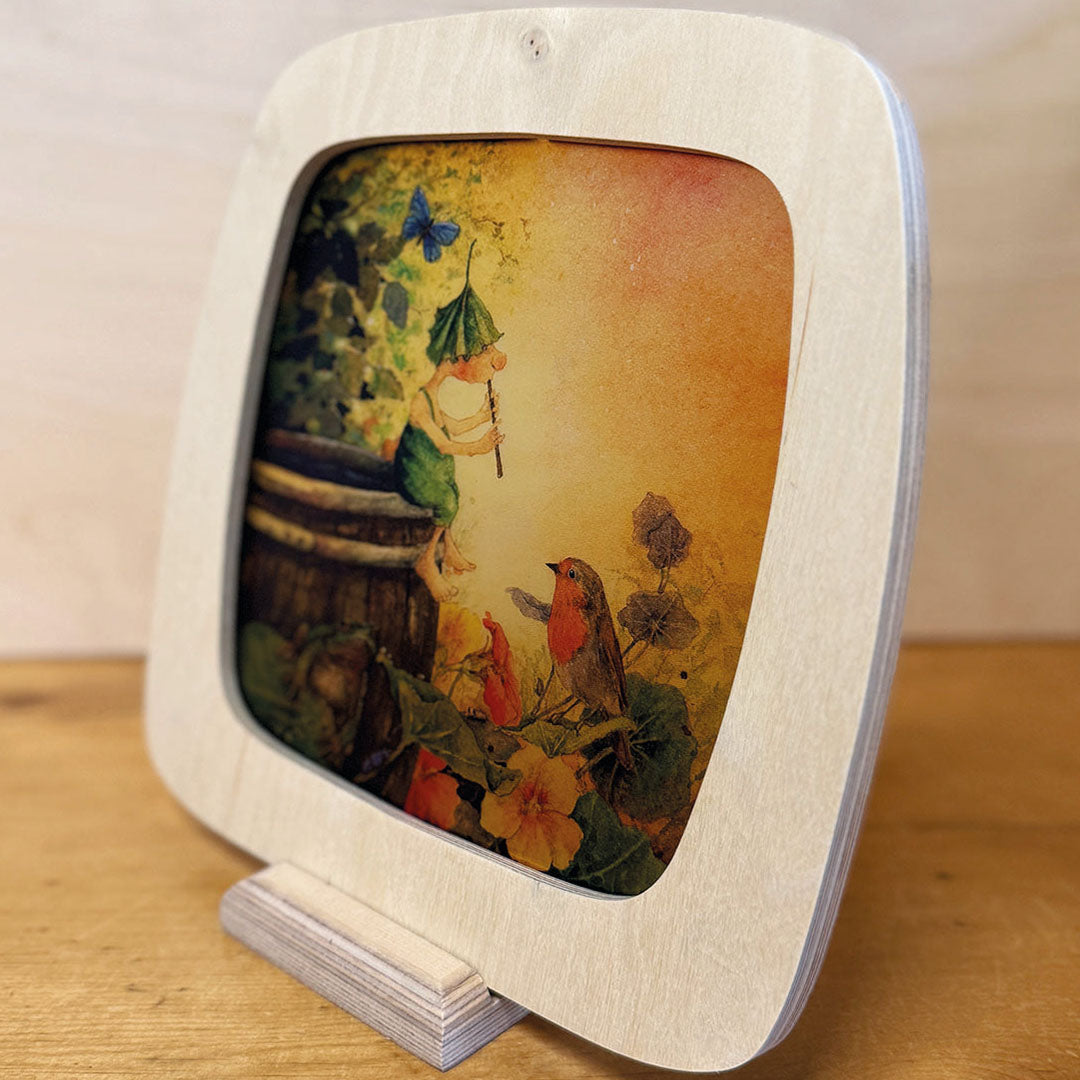 Houten toverplaat lijst met een illustratie van een elfje en een roodborstje, staand in een houten standaard.