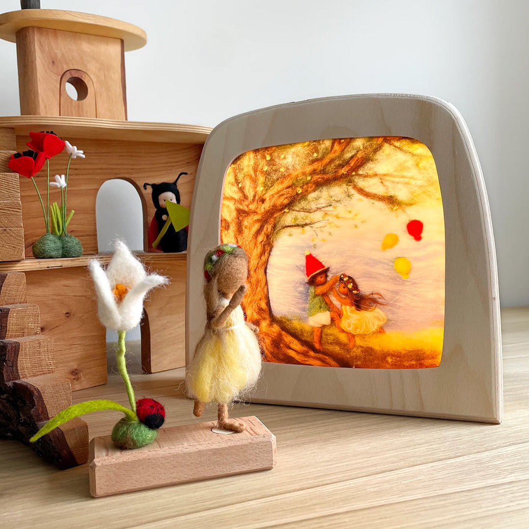 Toverlux toverlamp met een herfsttafereel van twee kinderen onder een boom, omringd door houten en vilten speelgoed.