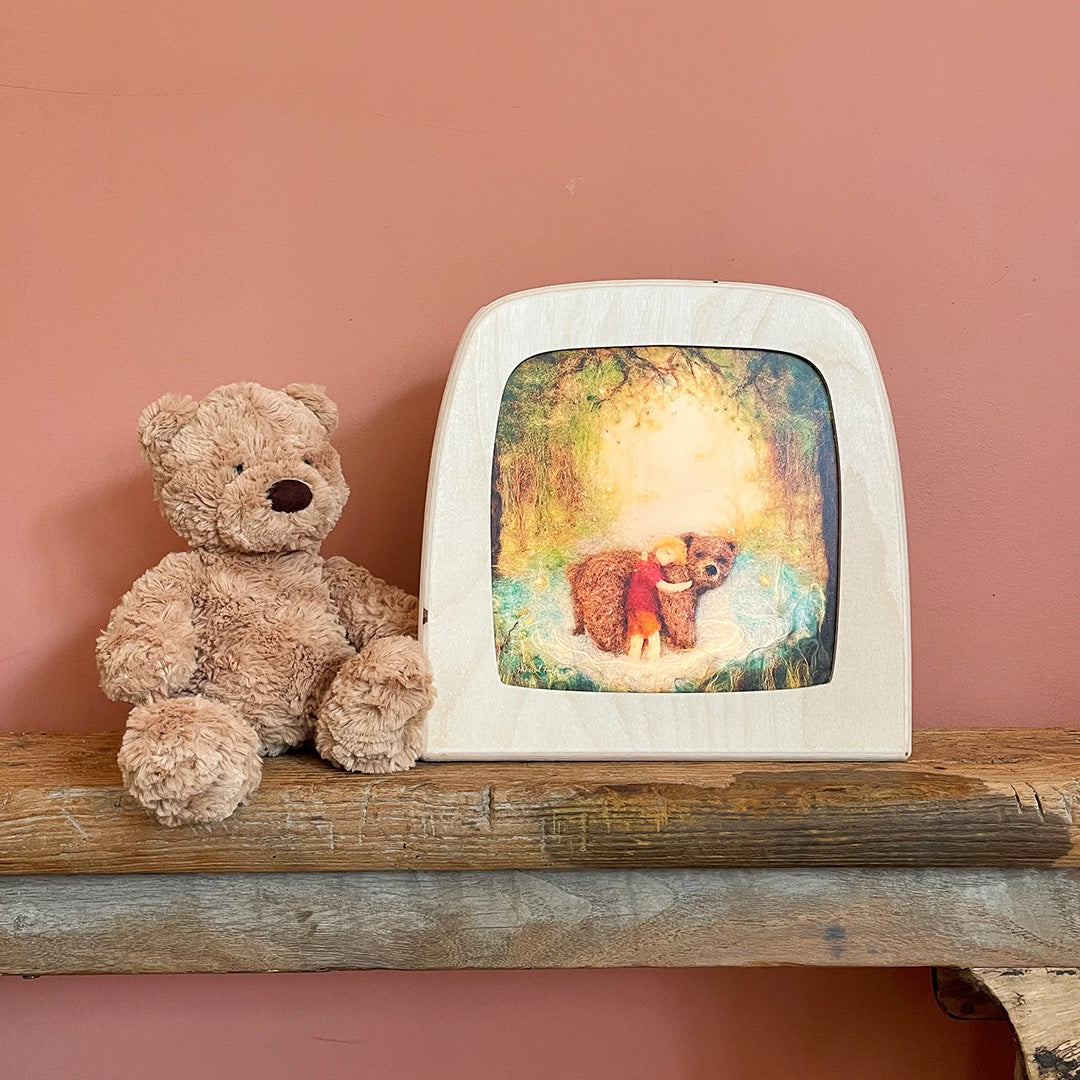 Toverlux toverlamp met een illustratie van een kind dat een beer knuffelt, naast een teddybeer op een houten plank.