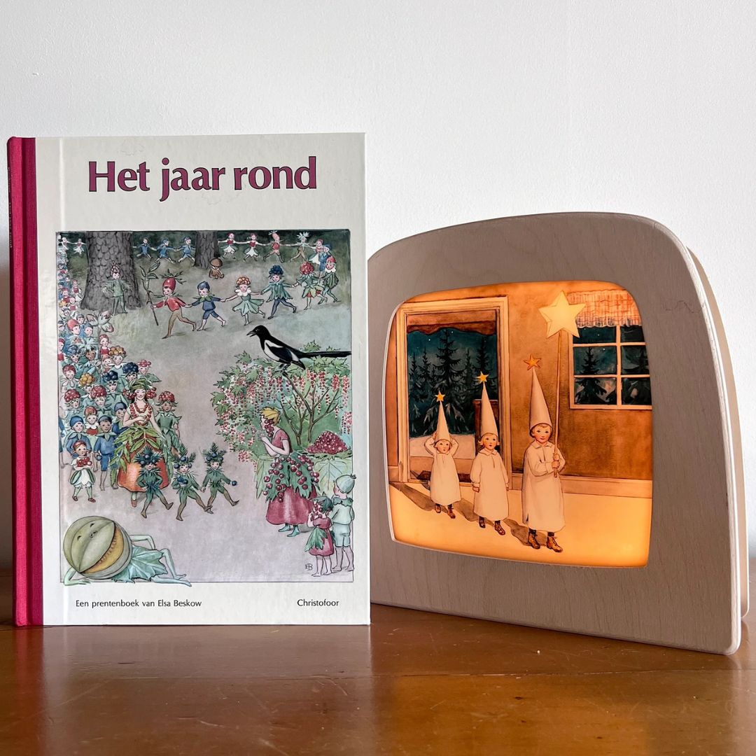 Een Toverlux toverlamp met de toverplaat van drie kinderen met sterren, naast het prentenboek 'Het jaar rond'.