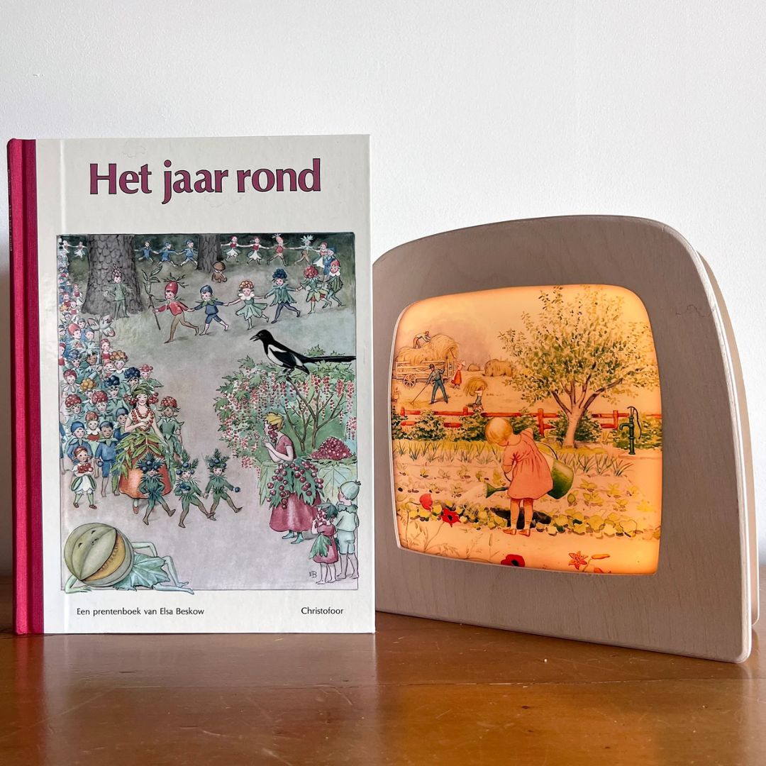 Een Toverlux toverlamp met de toverplaat van het meisje in de tuin, naast het boek 'Het jaar rond'.