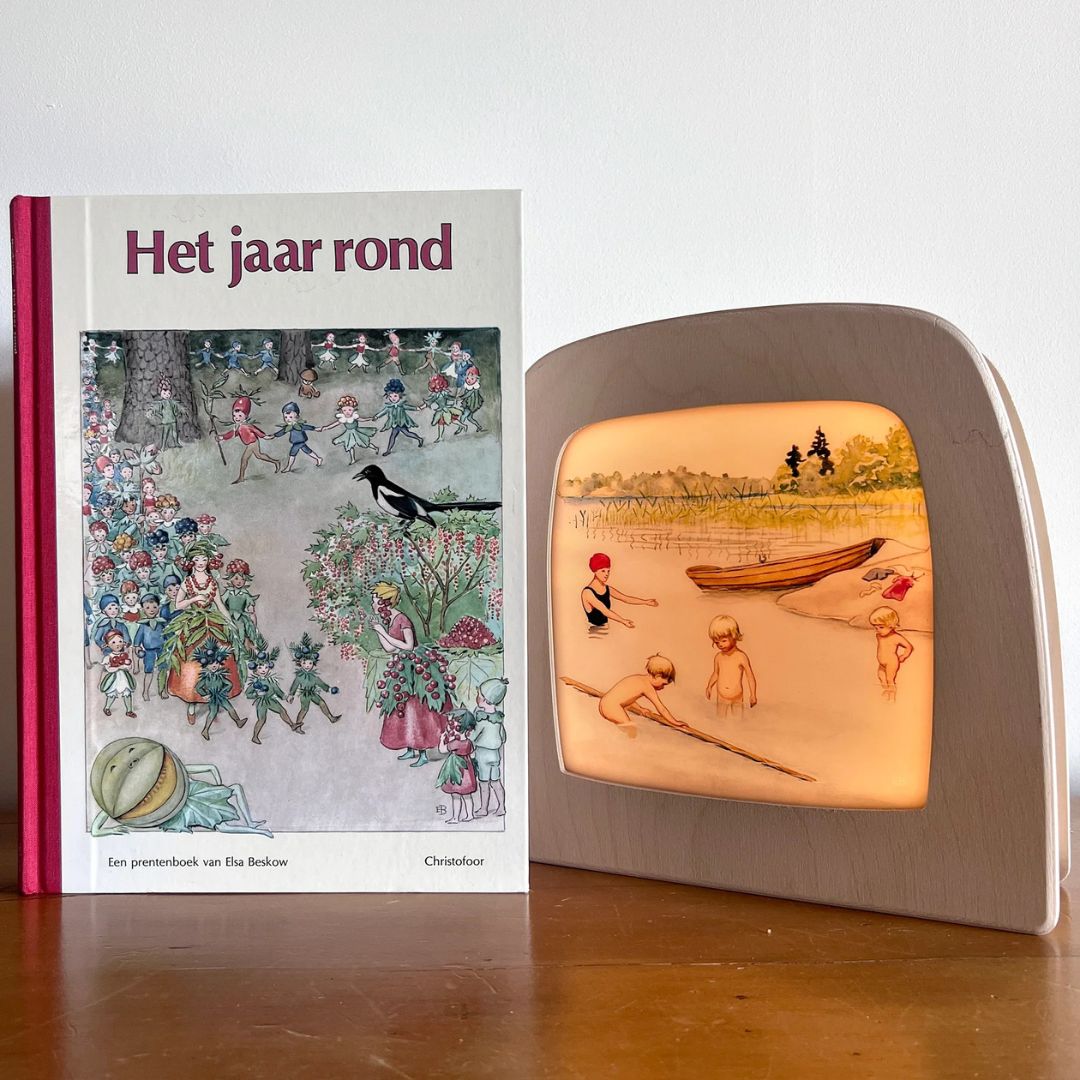 Toverlux toverlamp met de toverplaat van zwemmende kinderen naast het boek "Het jaar rond" van Elsa Beskow.