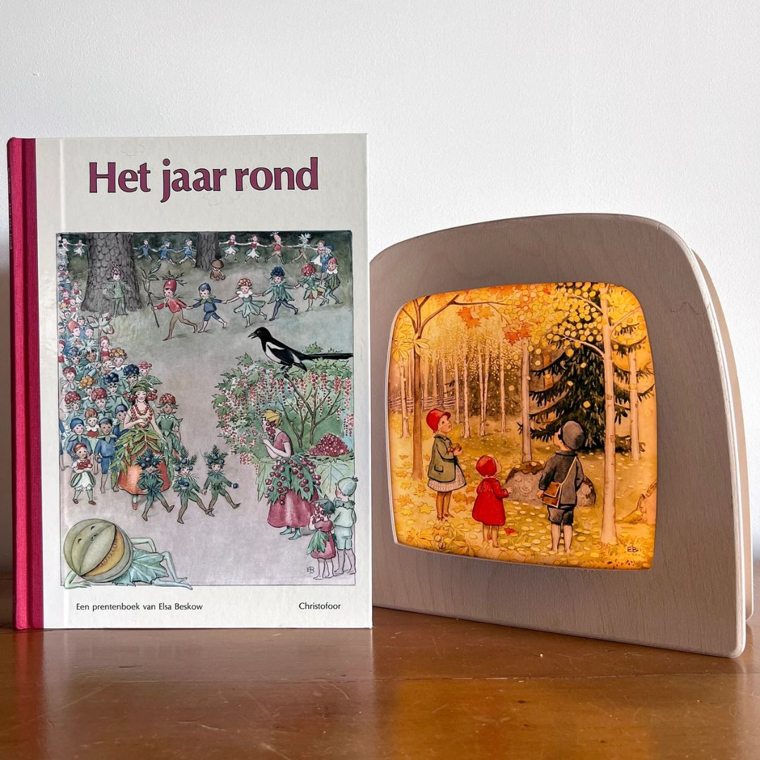 Een Toverlux toverplaat 'Het jaar rond - oktober' in een houten toverlamp naast het prentenboek 'Het jaar rond'.