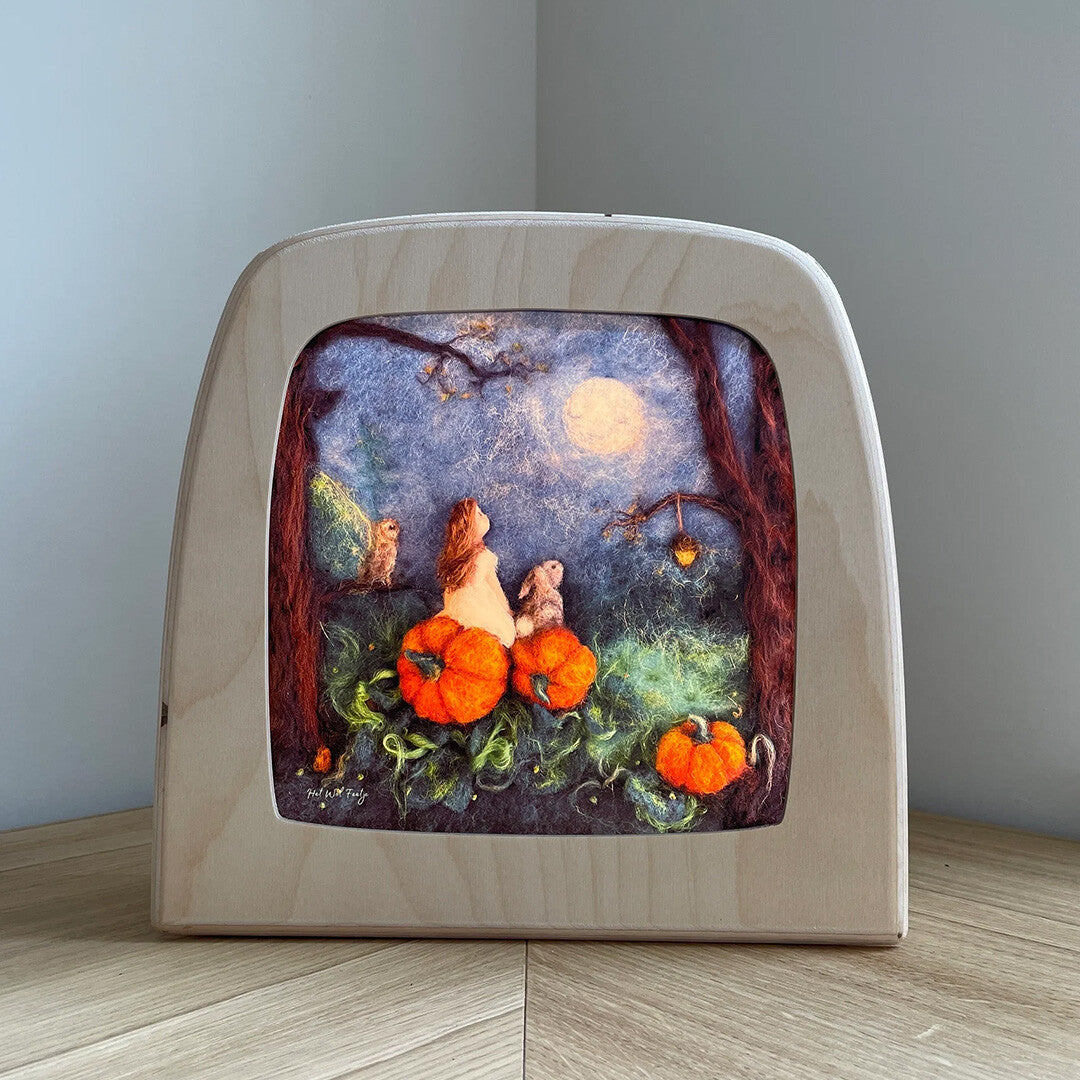 Vooraanzicht van de Toverlux toverplaat 'Moeder Maan' in een houten lampframe op een houten ondergrond.