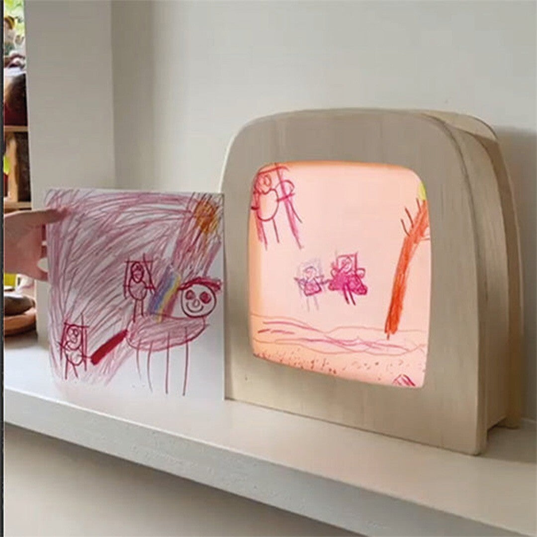 Een Toverlux toverlamp toont een kindertekening naast een ander vel papier met tekeningen.