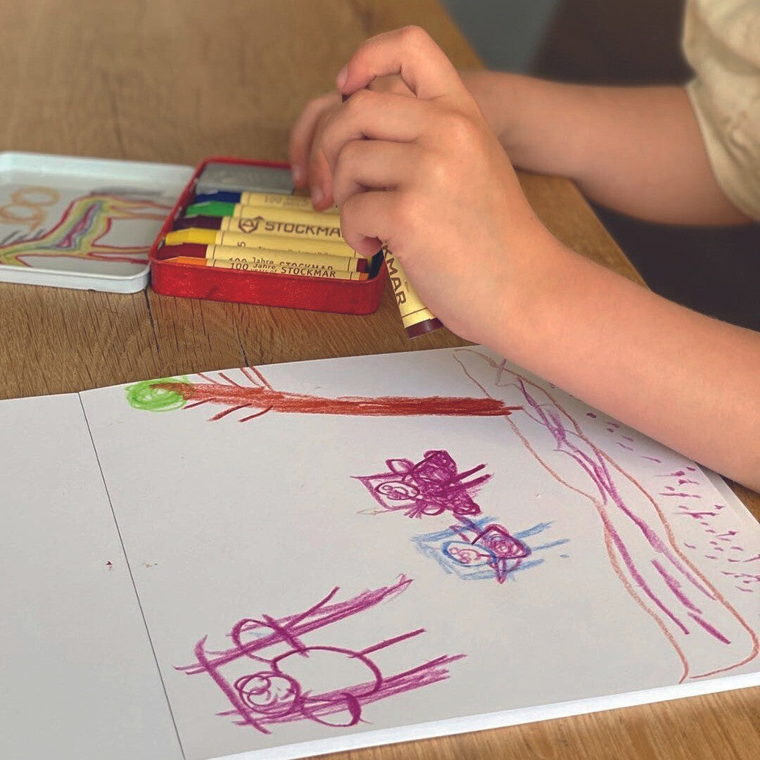 Kinderhanden tekenen met Stockmar waskrijtjes op papier.