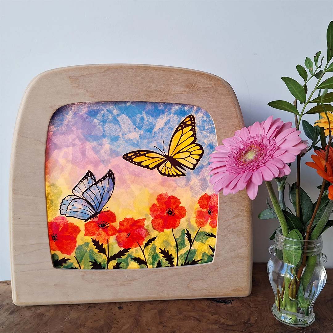Toverlux knutselwerk van vlinders en bloemen in een houten lijst, naast een vaas met bloemen.
