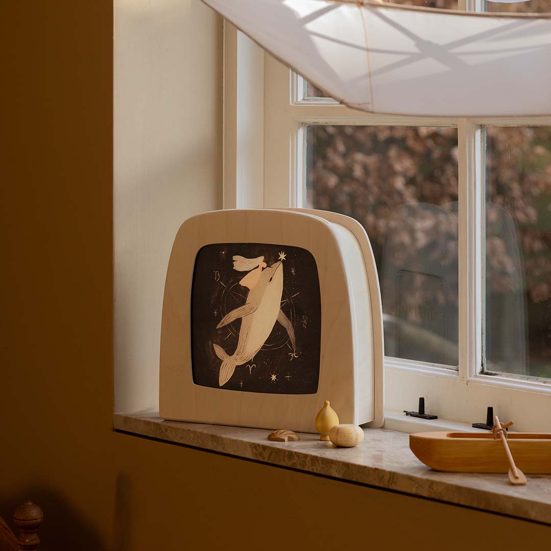 Toverlux toverlamp met de walvis toverplaat, staand op een vensterbank met andere houten speelgoedjes.