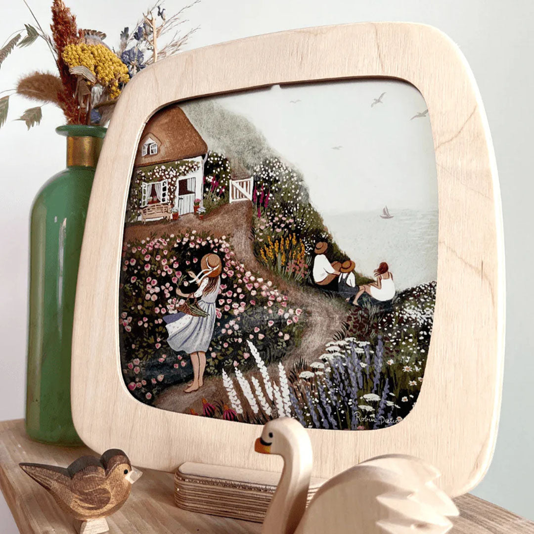 Houten lijst met een toverplaat van een huis aan zee met een bloeiende tuin en mensen.