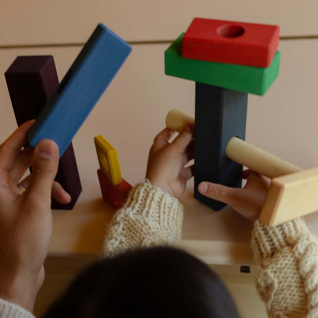 Twee paar handen, van een kind en een volwassene, bouwen met de veelkleurige toyto houten blokken.