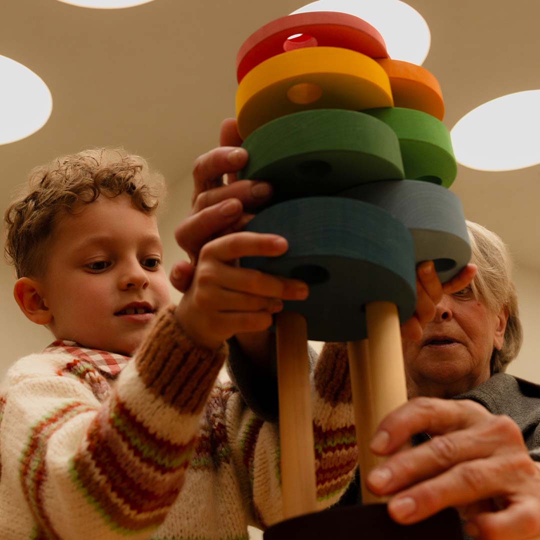 Een kind en een volwassene houden samen de hoge toyto houten stapeltoren vast.