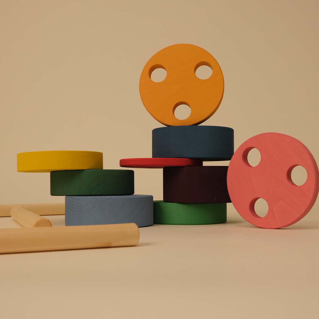 Losse onderdelen van de toyto houten stapeltoren, bestaande uit veelkleurige ronde schijven en houten pinnen.