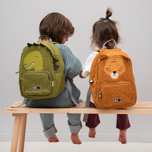 Twee kinderen zitten op een bankje, waarvan één de Trixie groene dino kleuterrugzak draagt.