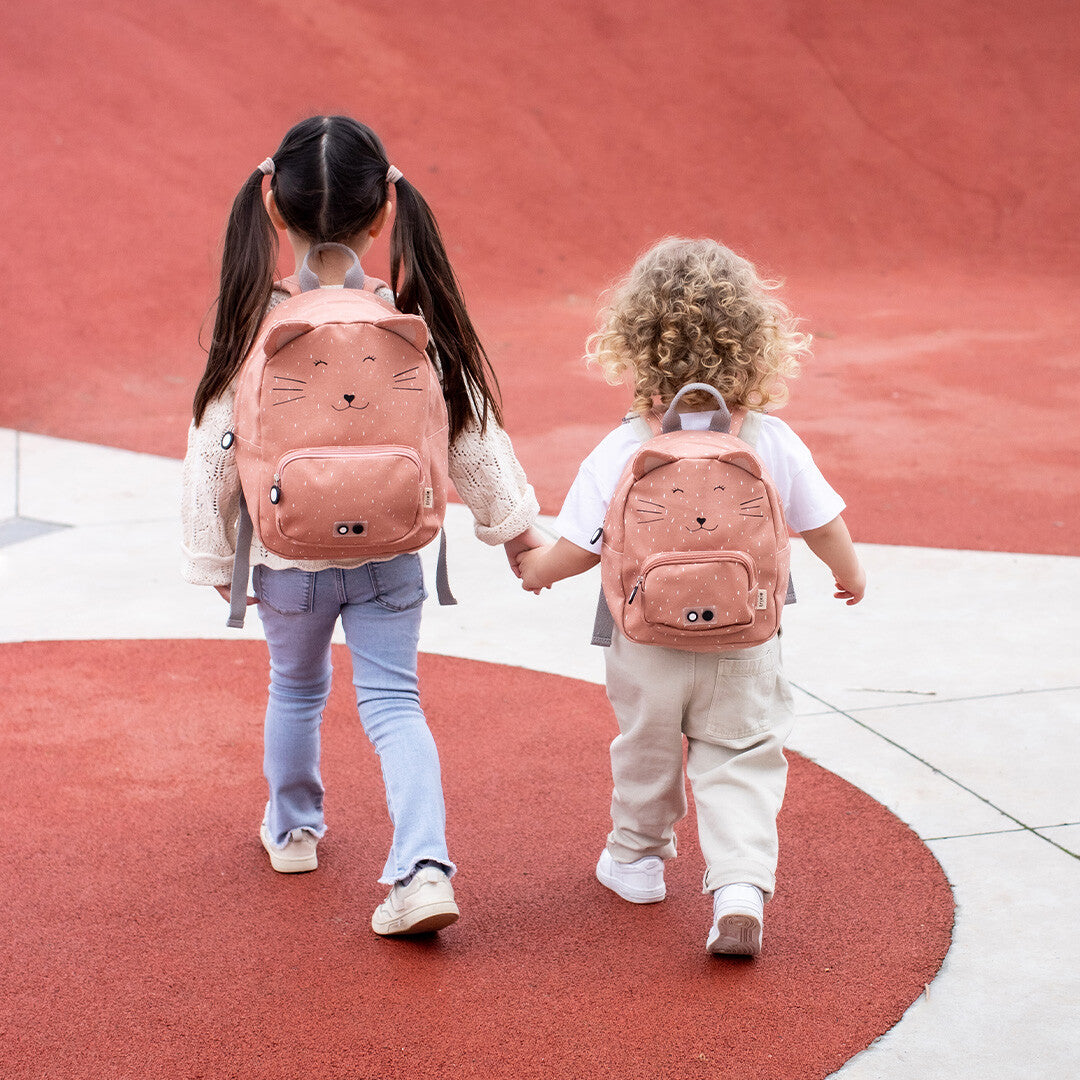Twee kinderen lopen hand in hand, beiden met een Trixie kleuterrugzak Mrs. Cat op hun rug.