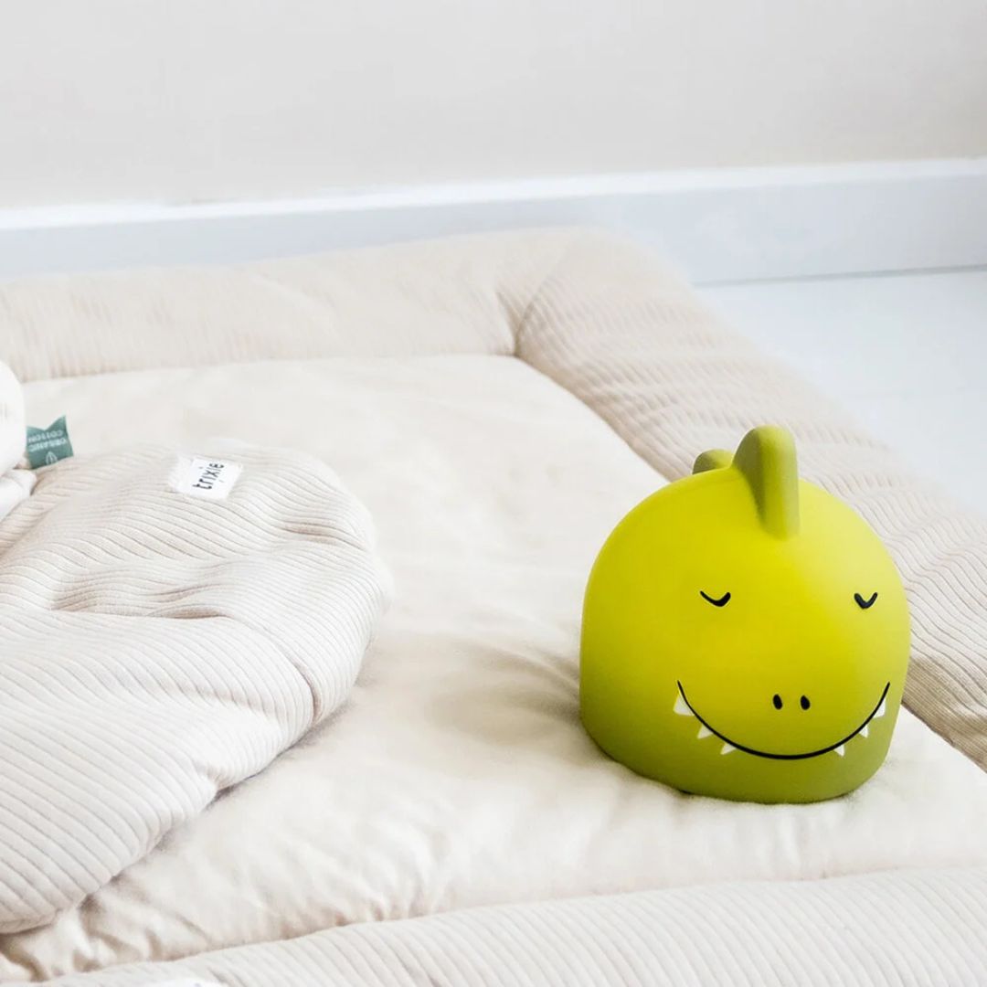 Trixie nachtlampje in de vorm van een groene dino op een crèmekleurige speelmat.