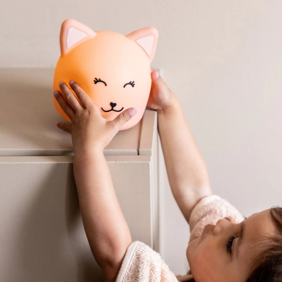 Een kind reikt naar het oplichtende Trixie katten nachtlampje op een kast.