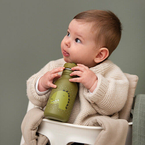 Een baby zit in een kinderstoel en houdt de Trixie groene kinder waterfles met dinosaurus patroon vast.