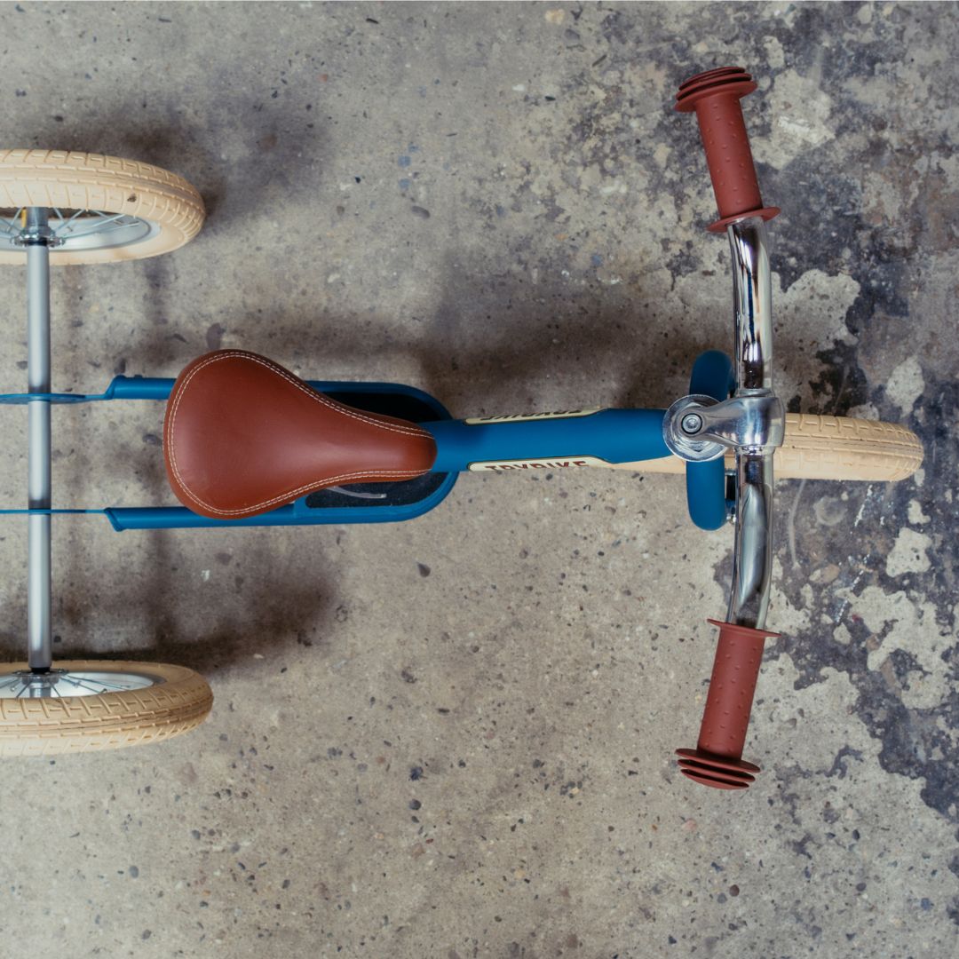 Trybike stalen 2-in-1 loopfiets in vintage blauw als driewieler, van bovenaf gezien op een betonnen ondergrond.