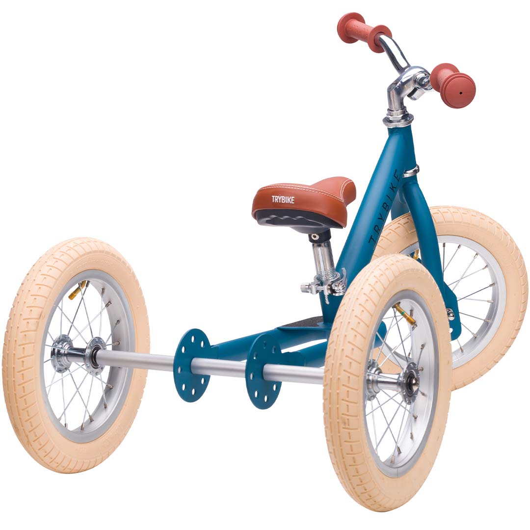 Trybike stalen driewieler in vintage blauw met bruin zadel en handvatten, schuin van voren.