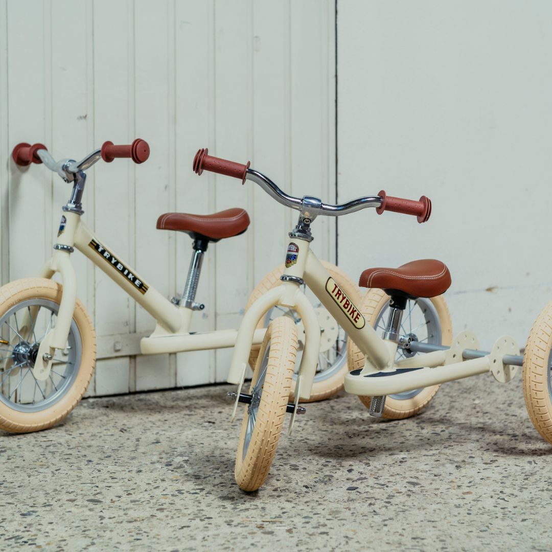 Twee Trybike 2-in-1 loopfietsen, één als tweewieler en één als driewieler, staan naast elkaar.