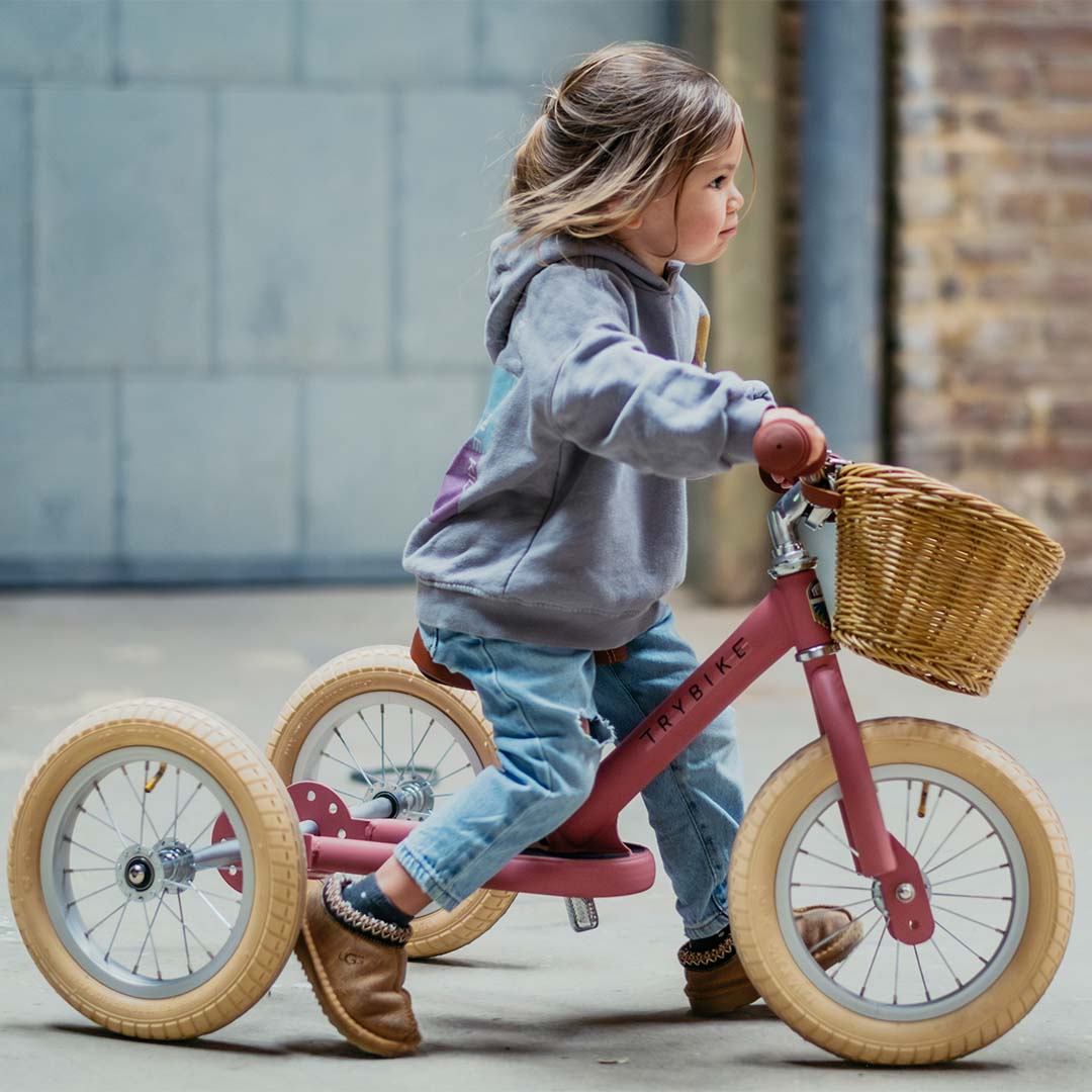 Een jong kind rijdt op de Trybike Steel 2-in-1 loopfiets in vintage roze als driewieler.