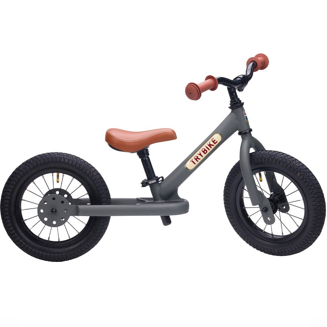 Trybike stalen loopfiets in matgrijs met bruin zadel en handvatten.
