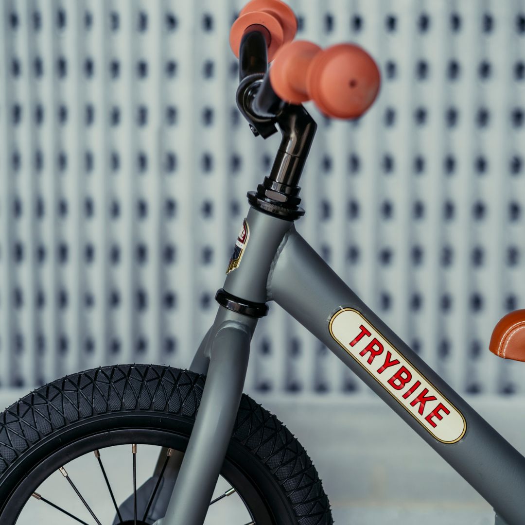 Detail van de Trybike stalen loopfiets met het logo op het frame en oranje handvatten.