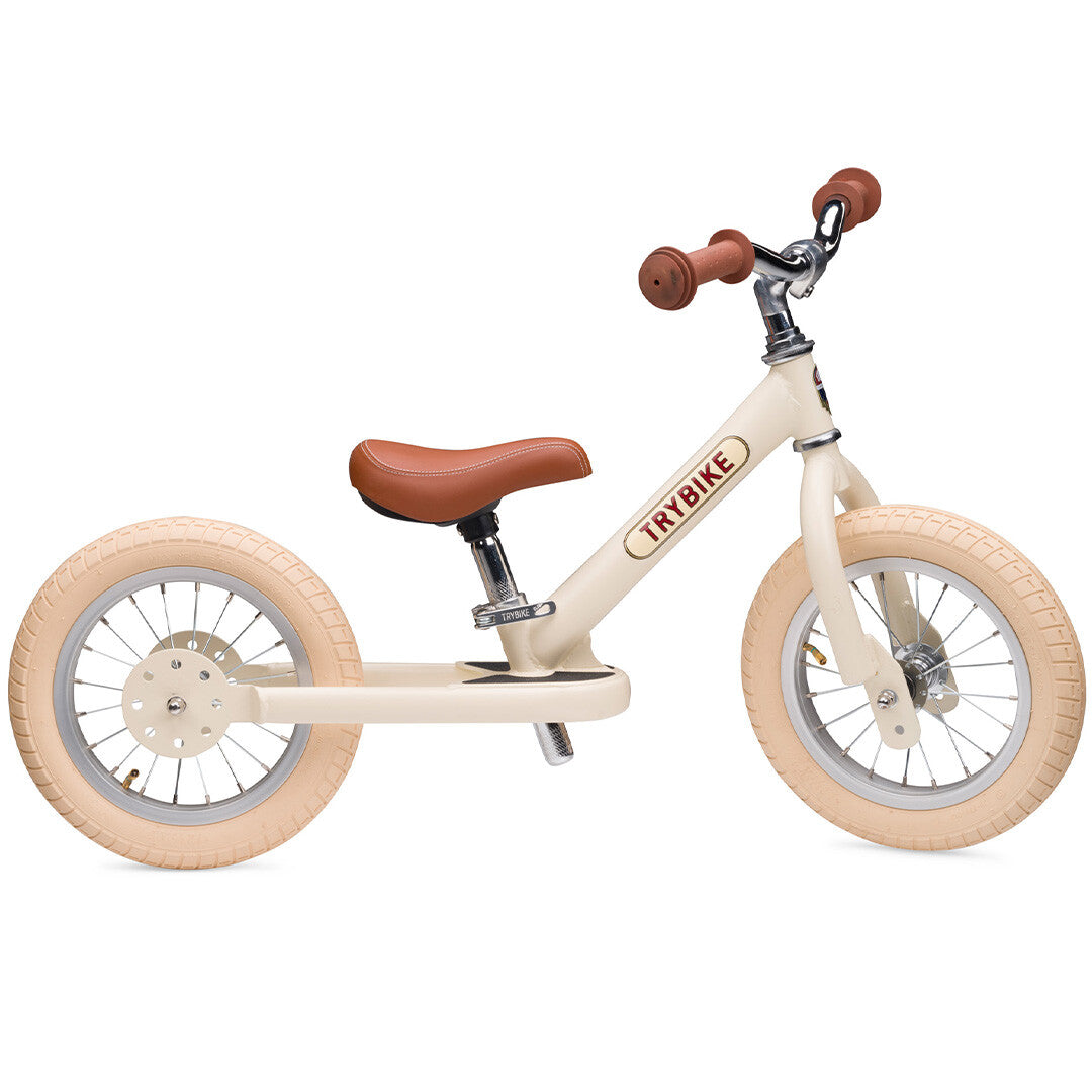 Trybike loopfiets in vintage cream met bruin zadel en handvatten, van de zijkant gefotografeerd tegen een witte achtergrond.