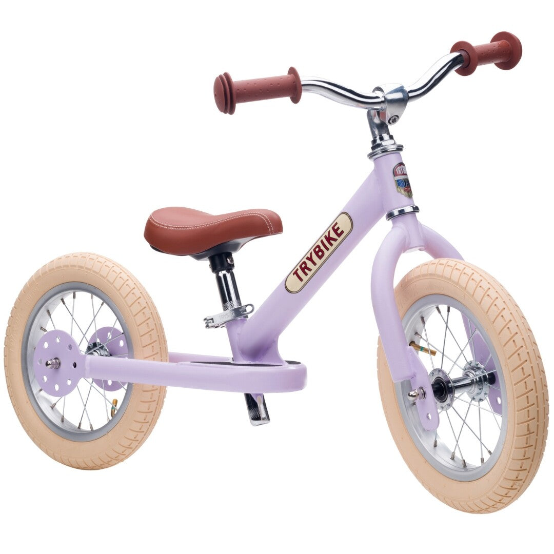 Trybike stalen loopfiets in vintage lila met bruine zitting en handvatten, op een witte achtergrond.