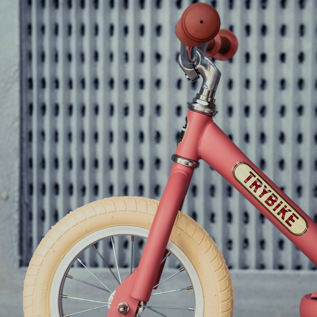 Detail van de Trybike vintage roze stalen loopfiets met het logo op het frame en een deel van het voorwiel.